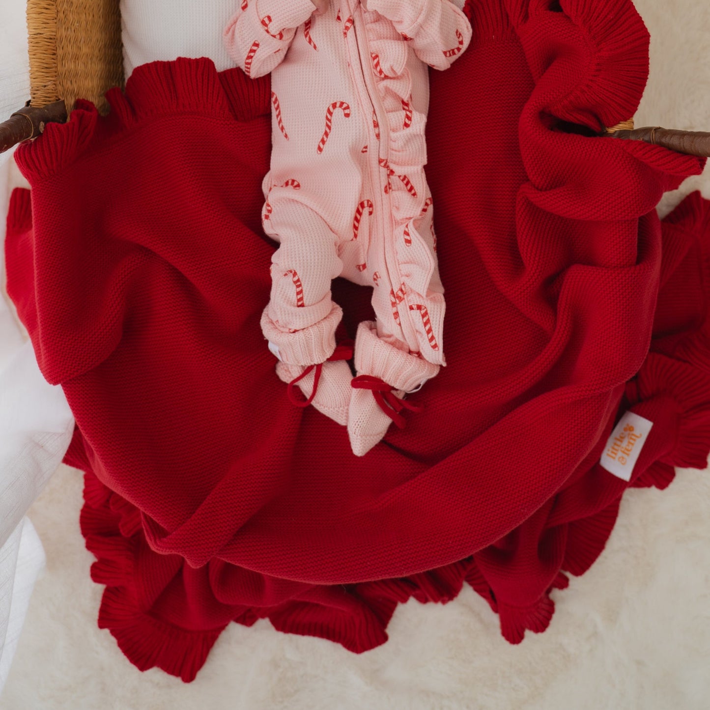 Baby in pink outfit and hat lying on red blanket inside a wicker basket