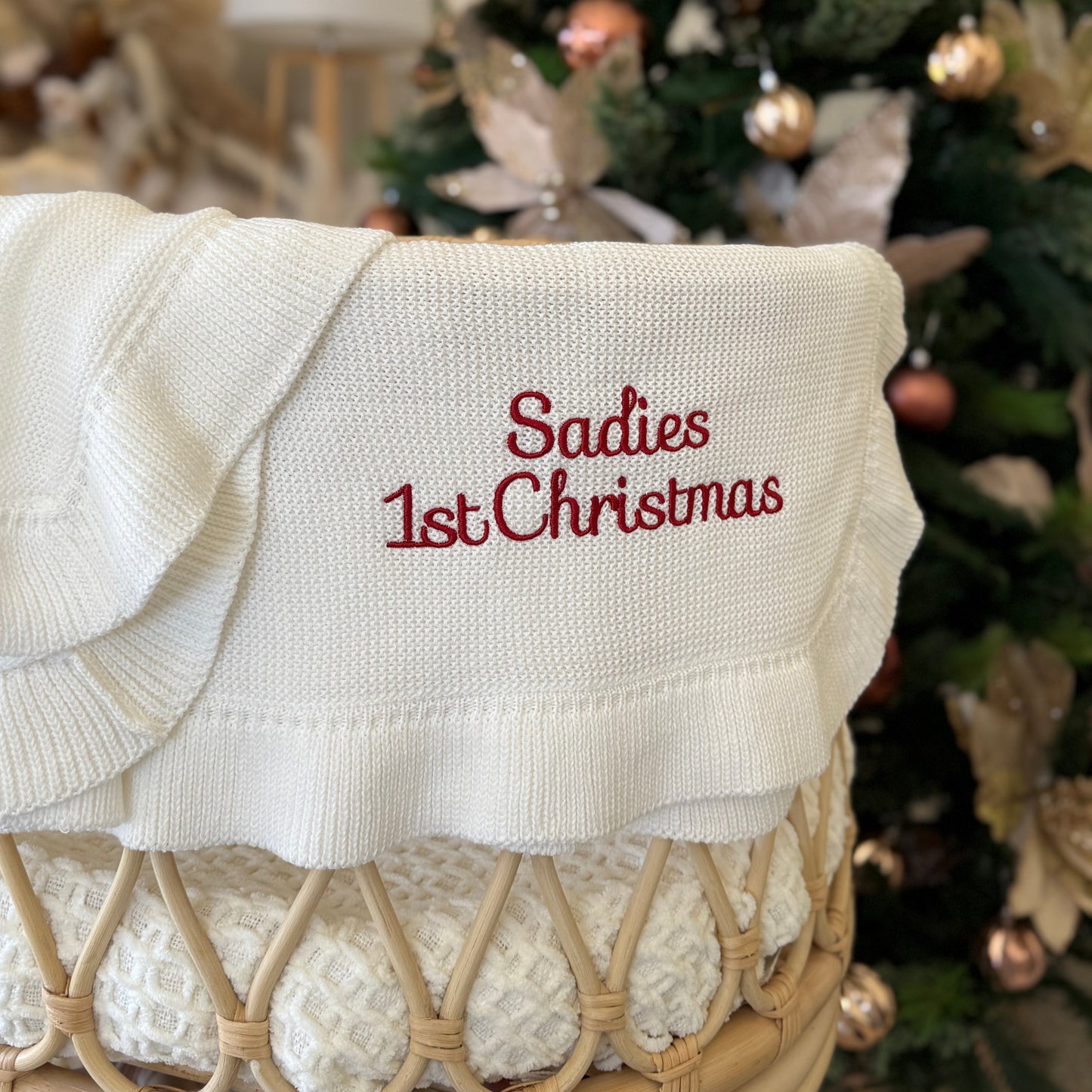 White blanket with 'Sadies 1st Christmas' embroidery in front of a decorated Christmas tree.