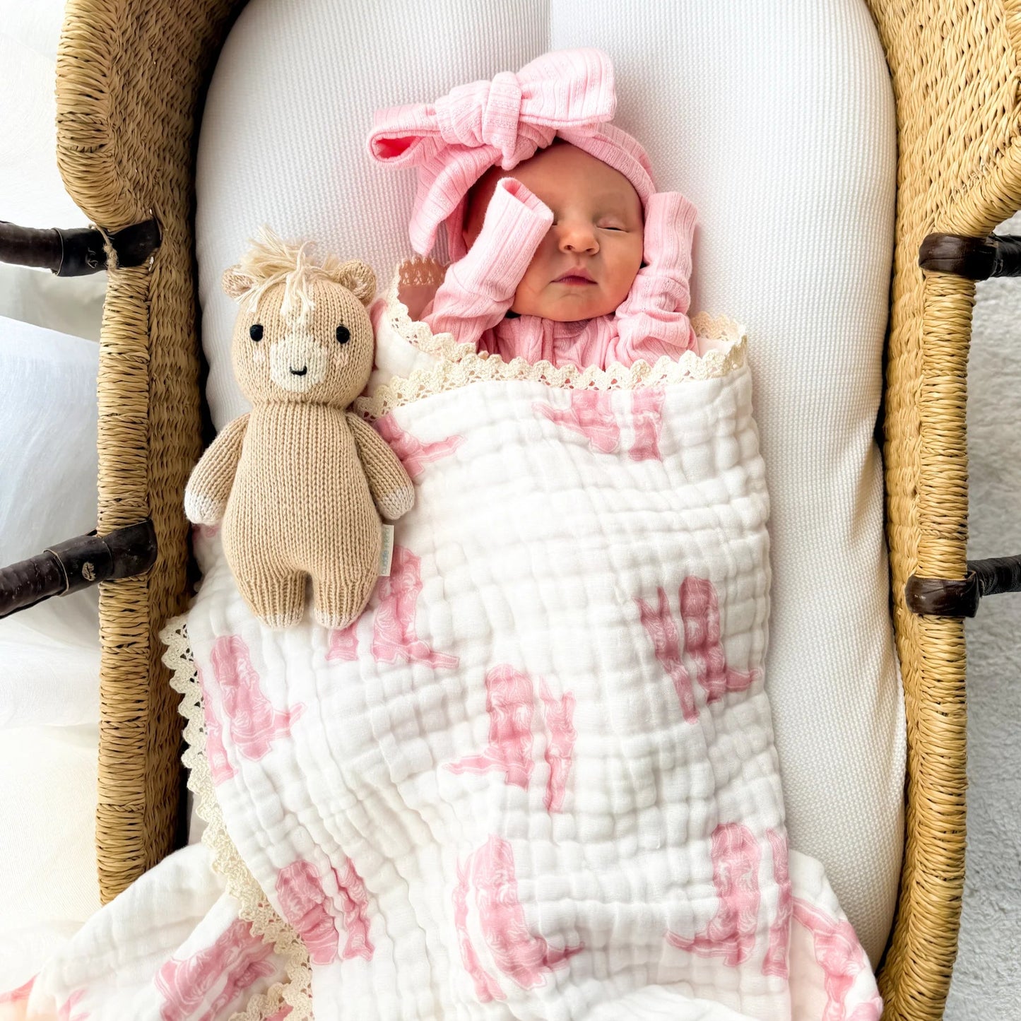 Newborn baby in a moses basket with a pink floral blanket and teddy bear.