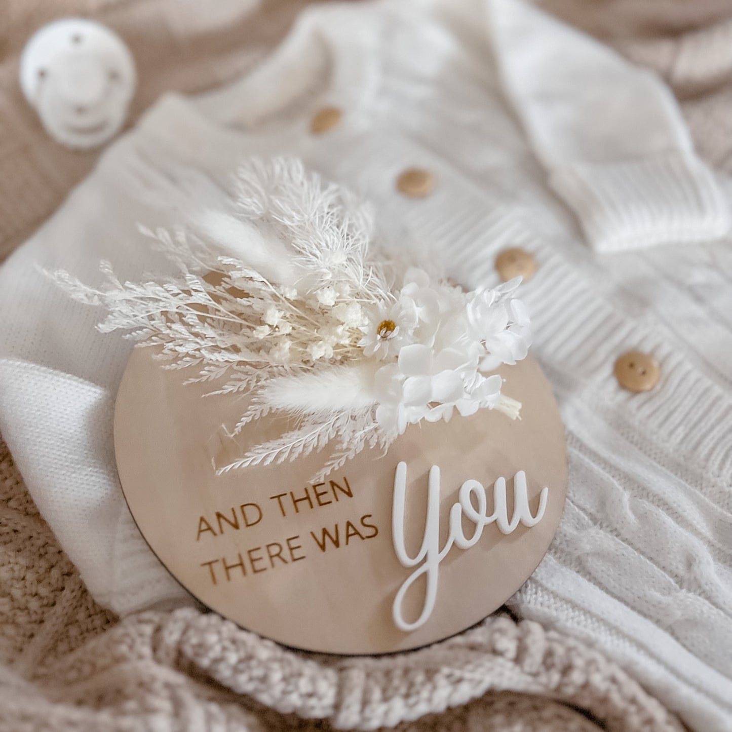 A wooden plaque with a dried floral arrangement on top, placed on a knit fabric, with the text 'And then there was you' printed on it.