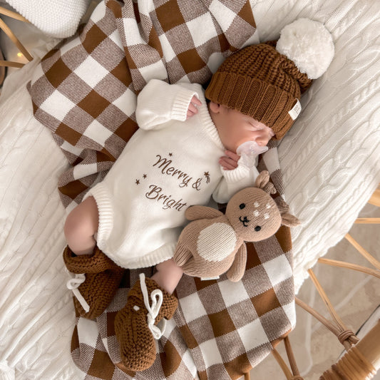 Newborn baby in a cozy setting with a checkered blanket and knitted hat. Merry & Bright Christmas knit romper and reindeer teddy