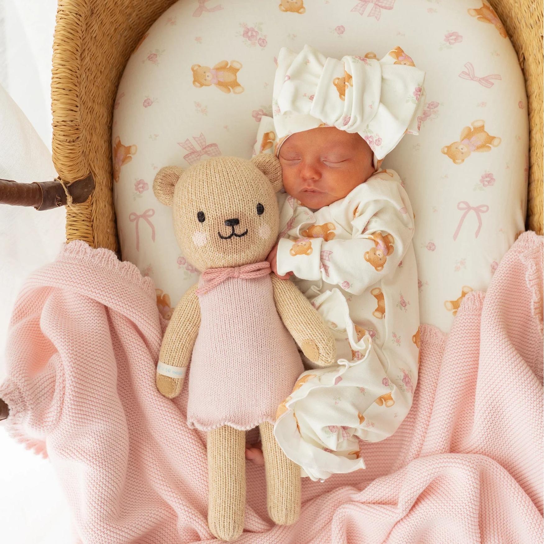 Newborn baby in a crib with a teddy bear and pink blanket