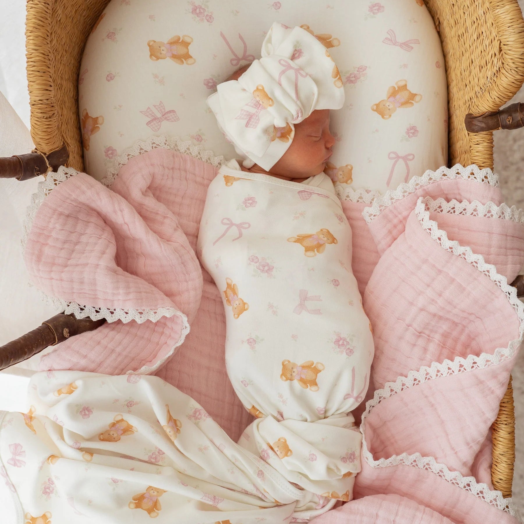 Newborn baby wrapped in a TEDDY BEAR & BOW pattern with pink blanket in a wooden crib.