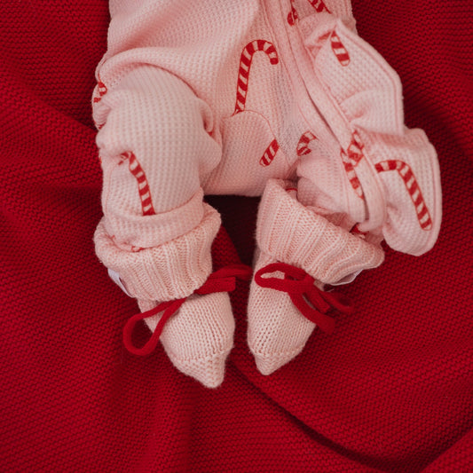 Pink baby socks with candy cane patterns on a red fabric background