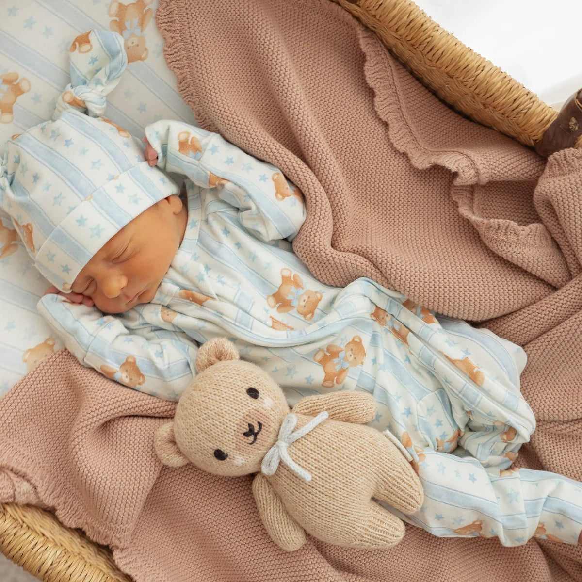 Newborn baby in a crib wearing a blue teddies romper with a teddy bear, wrapped in a blanket.
