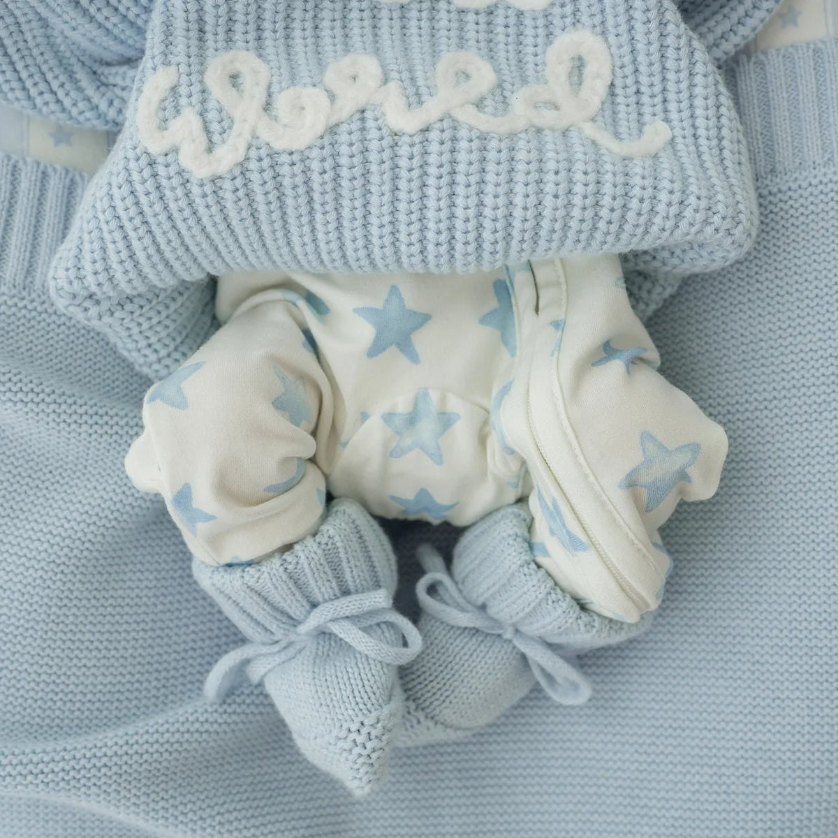 Baby blue and white baby outfit with booties, pants, and hat on a soft fabric background