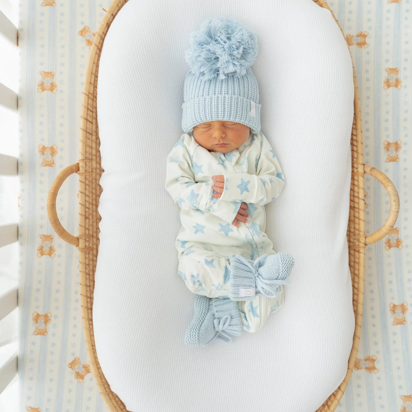 Newborn baby in a Moses basket wearing a blue knitted hat and matching outfit.