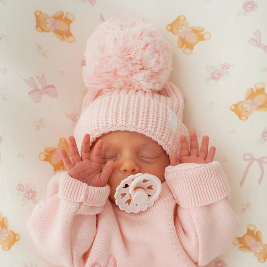 Newborn baby in pink outfit with matching hat on a patterned background