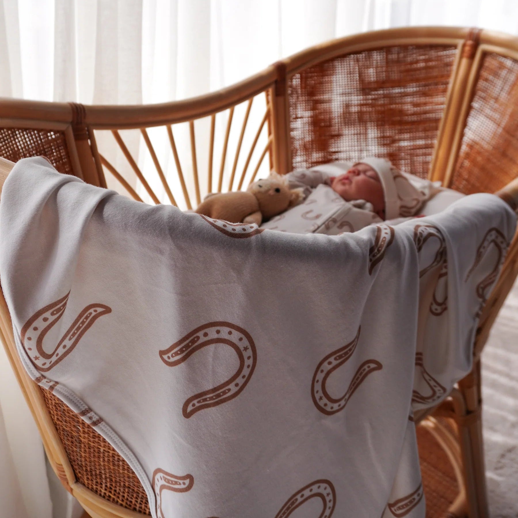 Baby wrapped in a blanket with horse shoe pattern on a wicker chair.