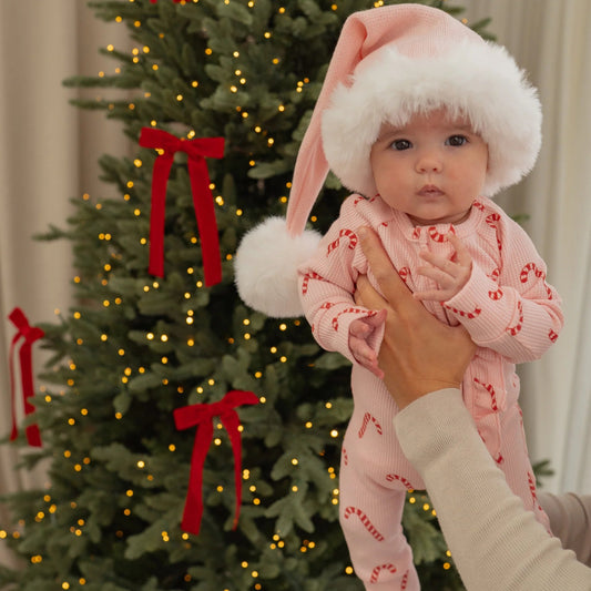 Baby in a festive outfit being held in front of a decorated Christmas tree.