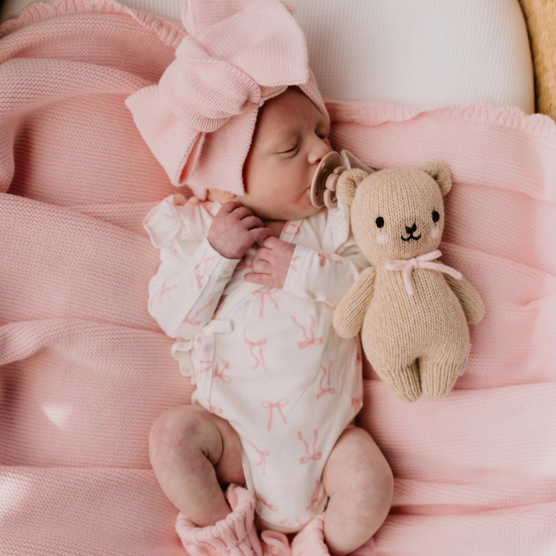 Newborn baby in pink outfit with a teddy bear, wrapped in pink blanket