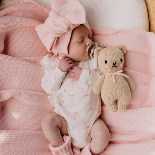 Newborn baby in pink outfit with a teddy bear, wrapped in pink blanket