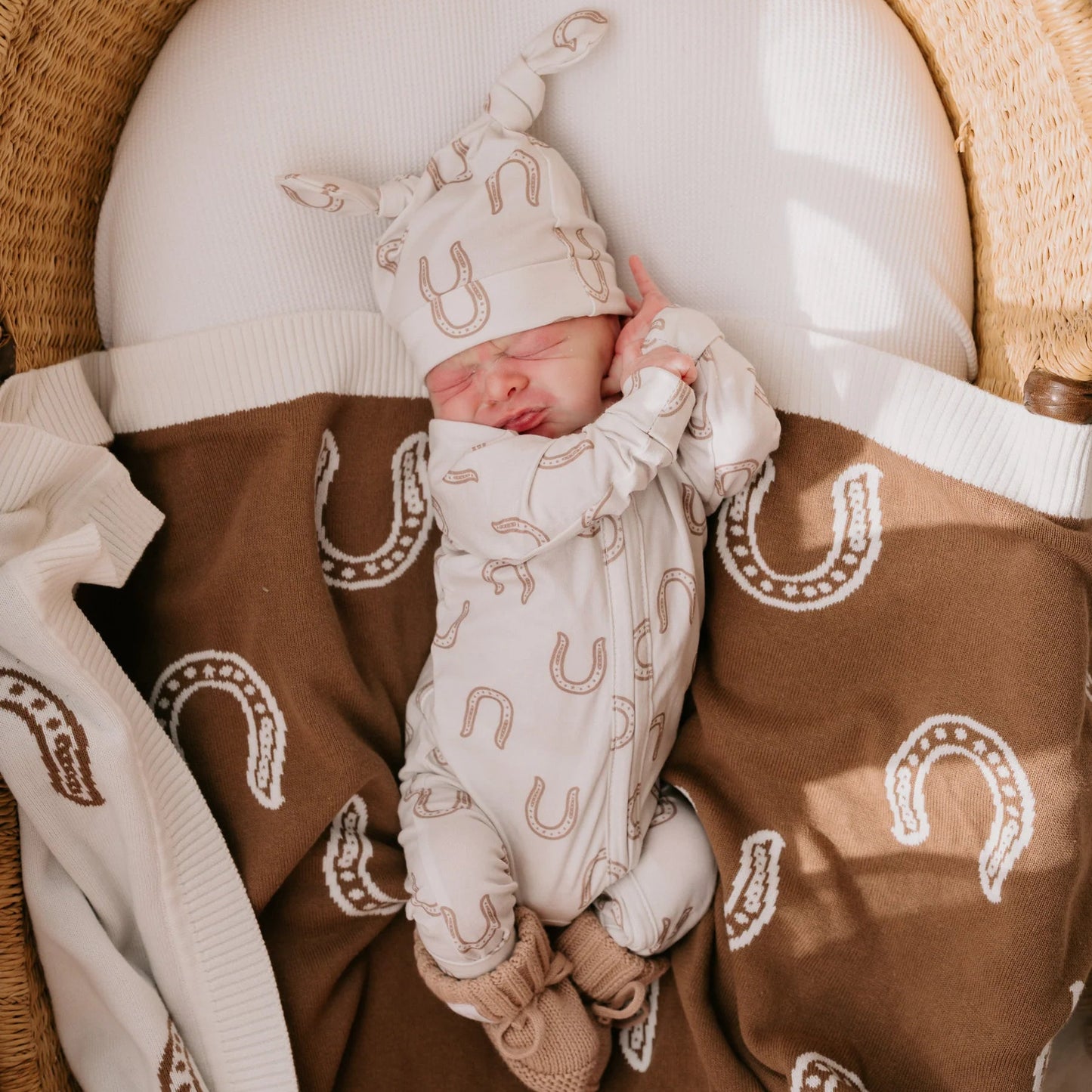 Newborn baby in a crib with a brown blanket featuring horse shoe patterns