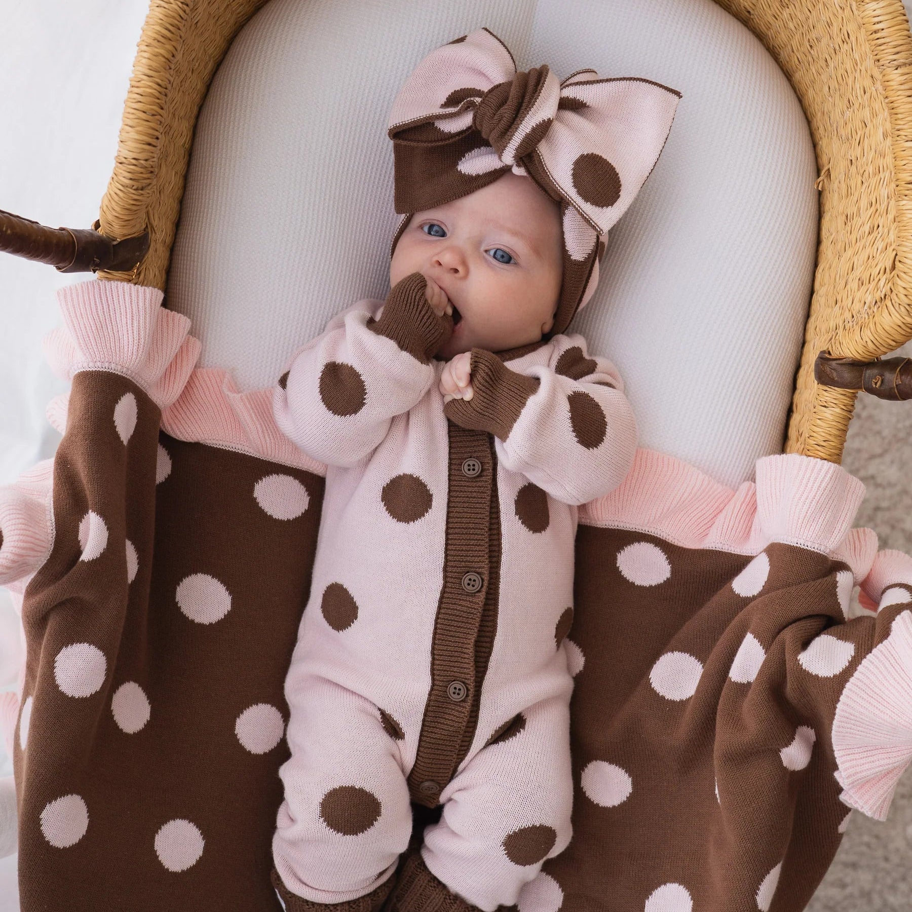 Baby in a polka dot outfit with a large bow in a crib