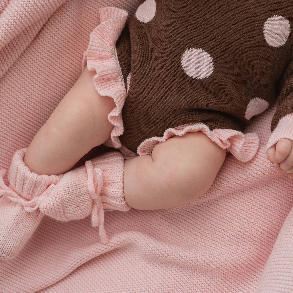 Baby legs in pink booties and a brown outfit with pink polka dots on a pink blanket