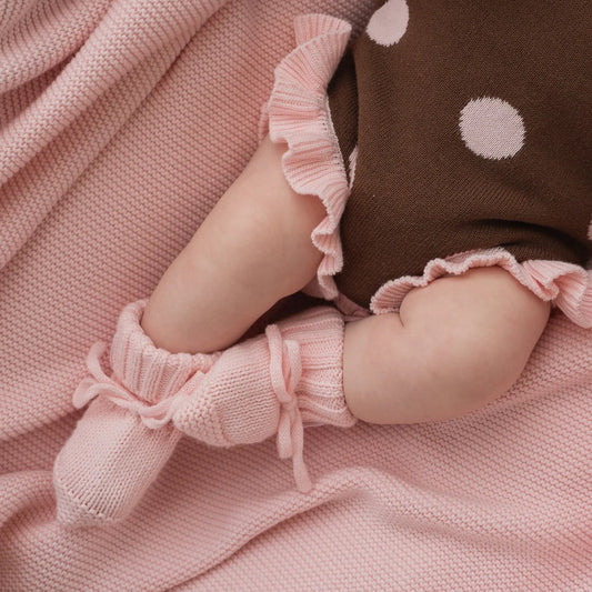 Baby legs in pink booties and a brown outfit with white polka dots on a pink blanket