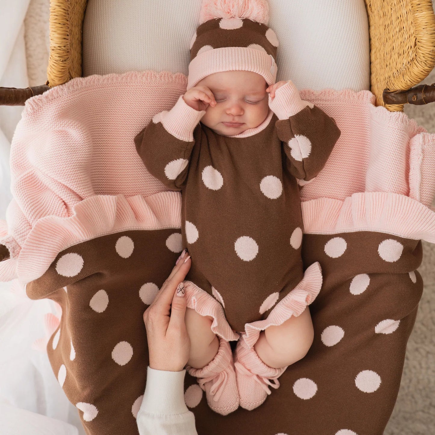 Baby in a brown polka dot outfit with pink accents lying in a wicker basket.