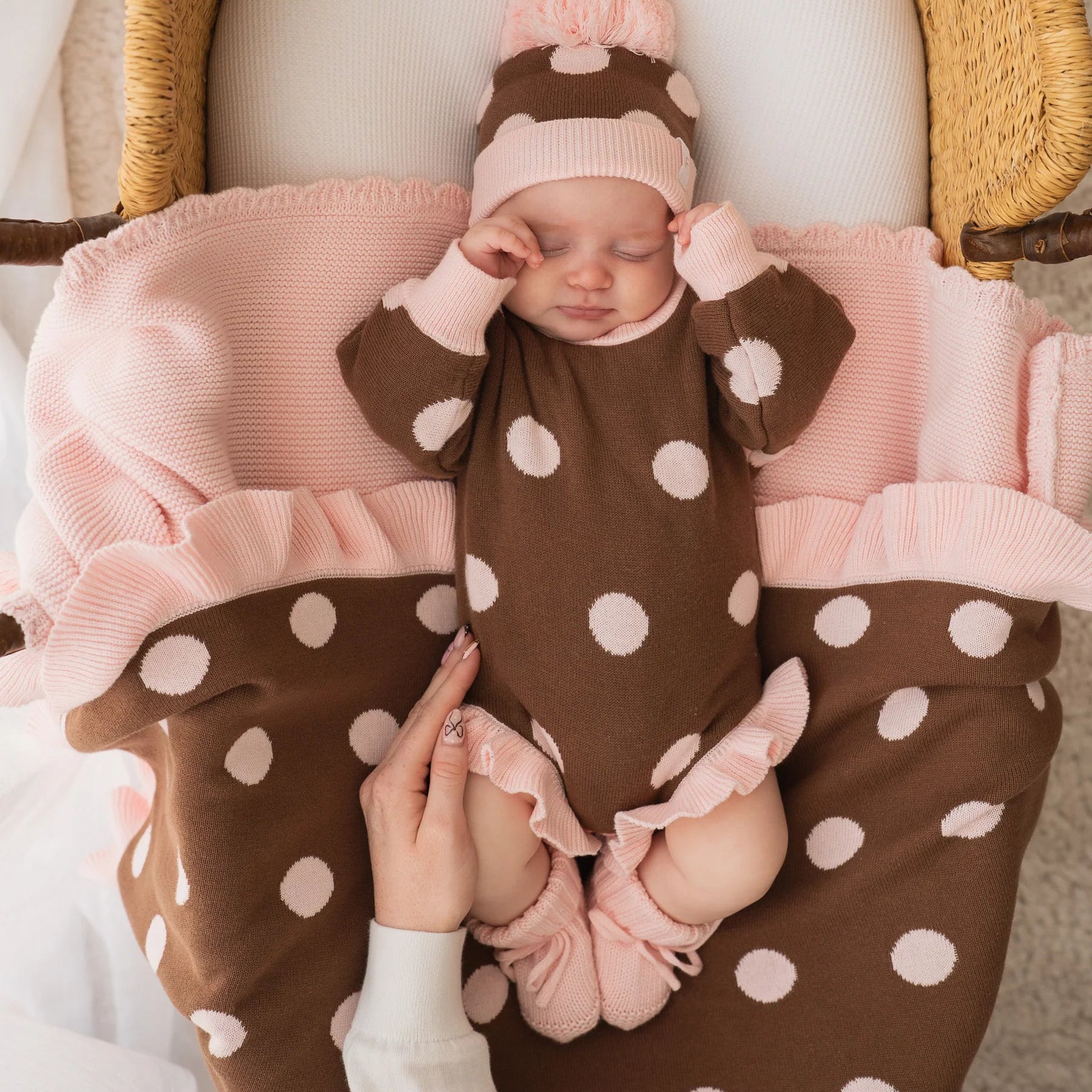 Baby in a brown polka dot outfit with pink accents lying in a wicker basket.