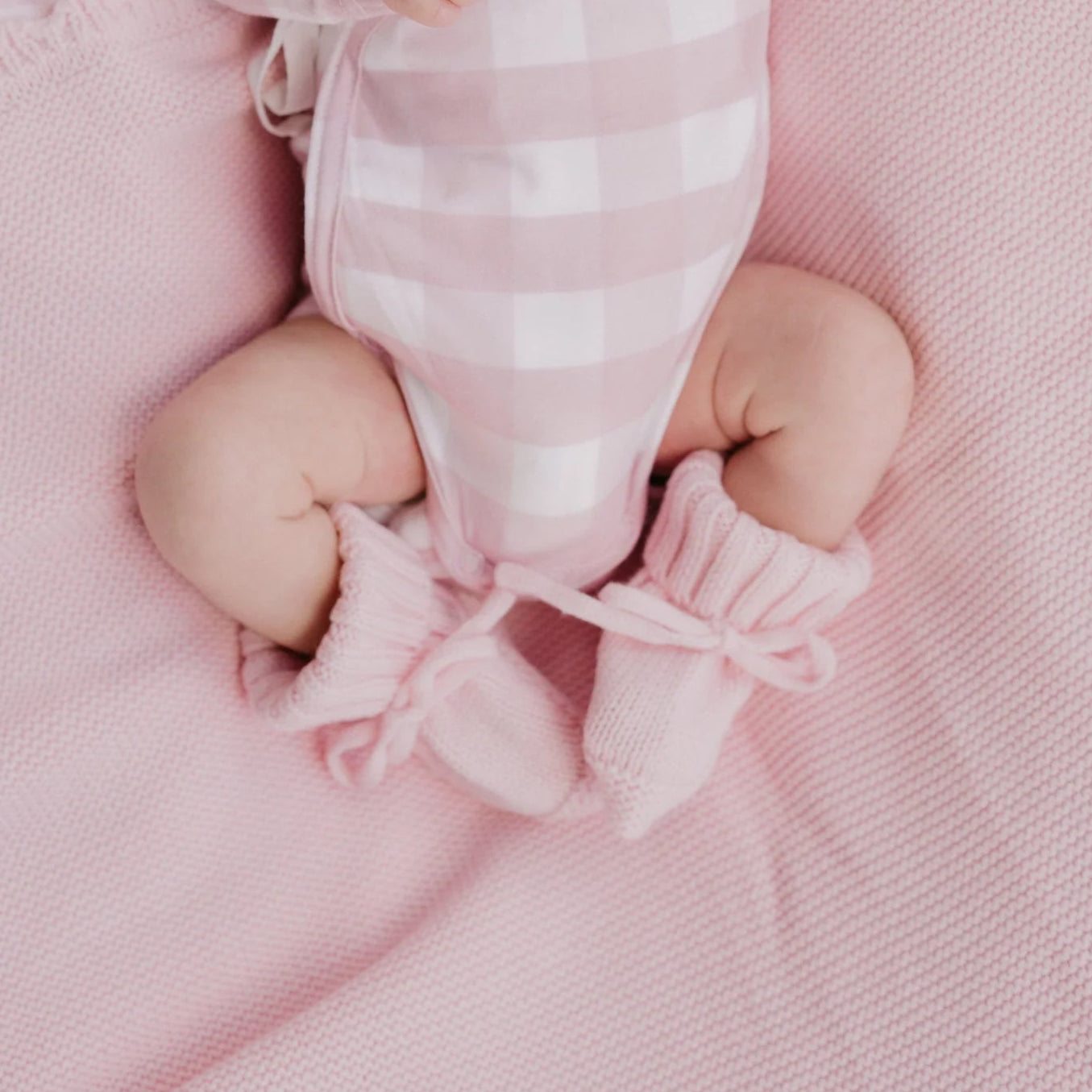Newborn baby in pink outfit and hat lying on a pink blanket