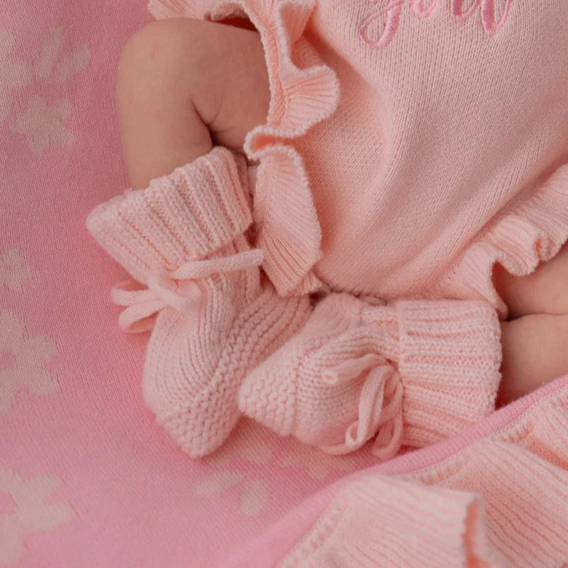 Baby outfit with pink ruffled romper and booties on a pink floral background