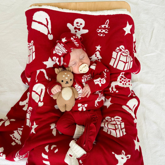 Baby in red pajamas with Christmas patterns lying on a matching red blanket.