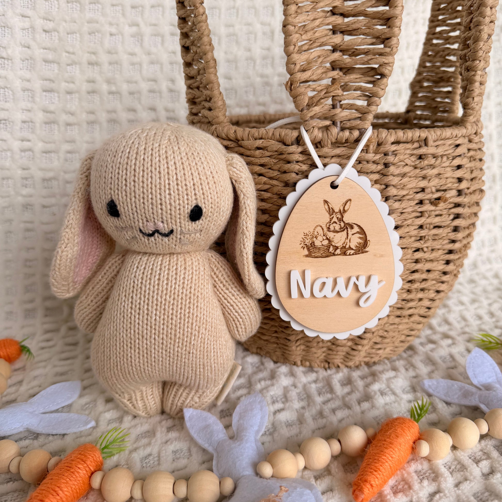 Knitted bunny toy with a woven bag and decorative elements on a textured surface, personalised easter basket name tag.