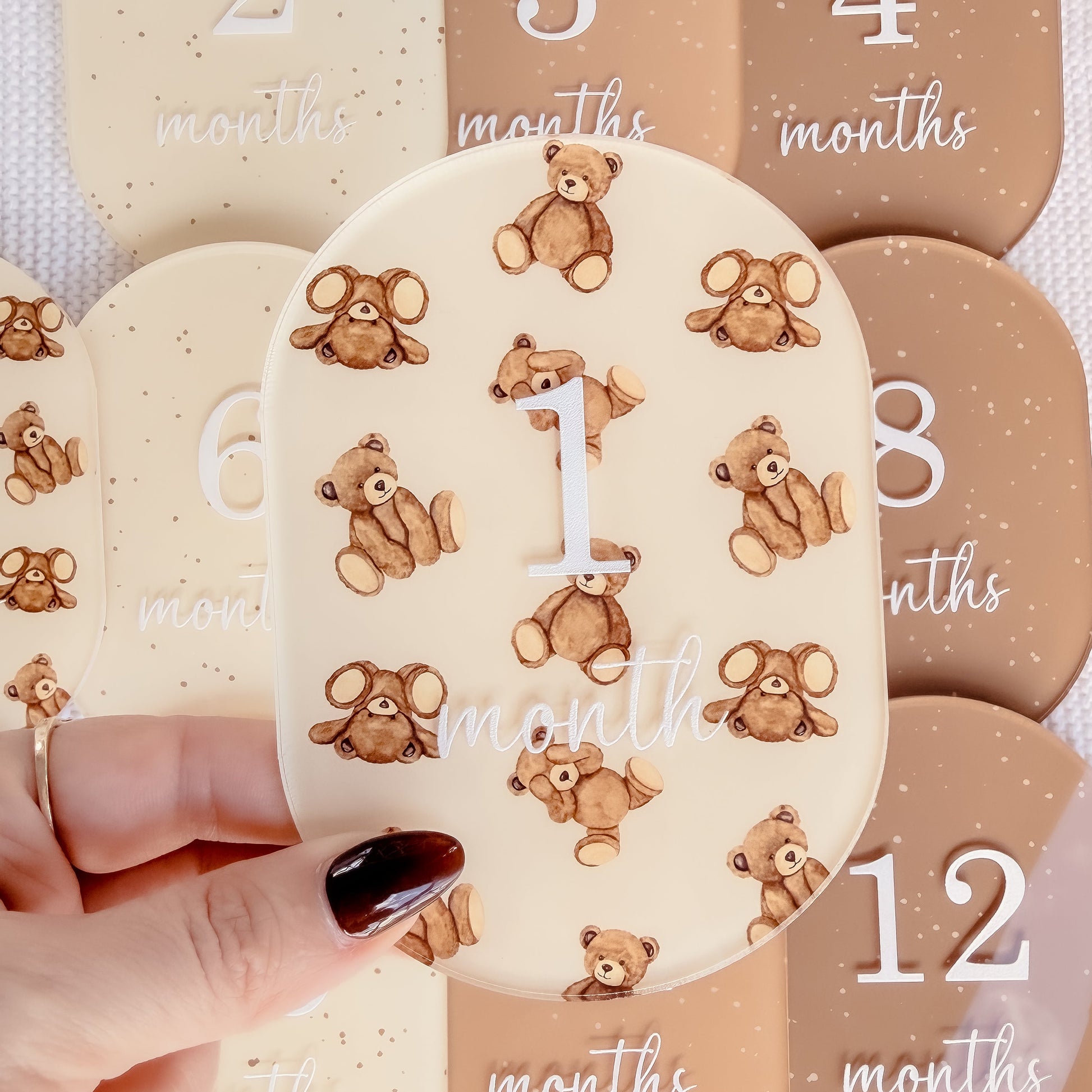 Baby milestone cards with teddy bear design and months printed on them, held by a hand.