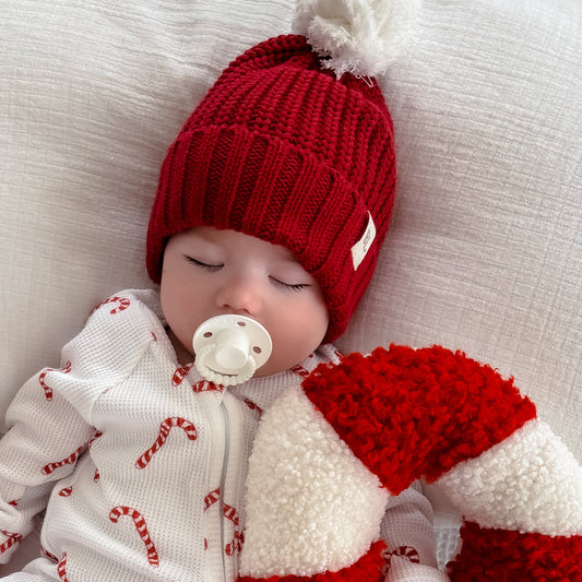 Newborn baby in a red and white outfit with a candy cane-shaped pillow