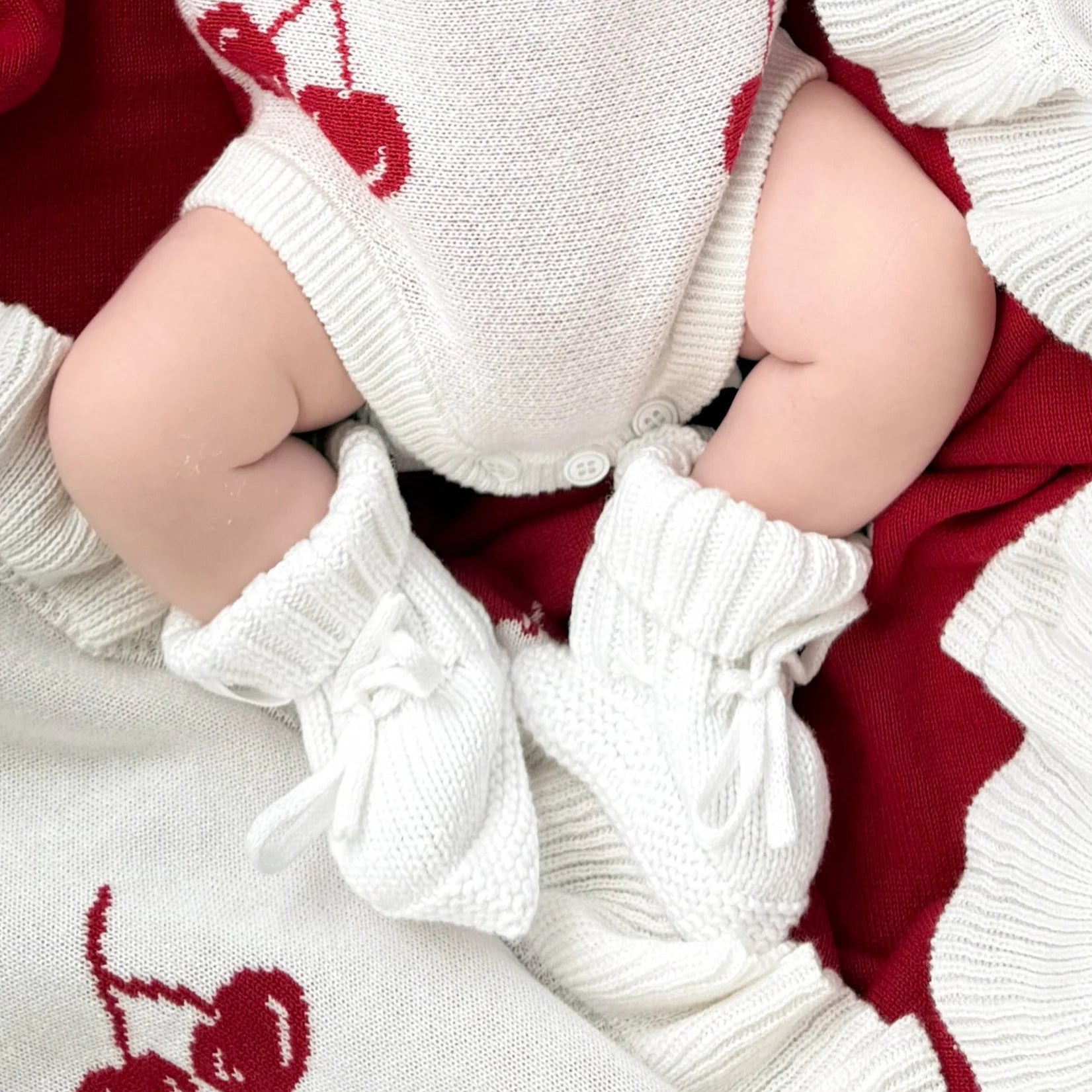 Baby in a red and white outfit with cherry patterns, white knitted booties