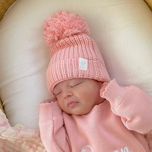 Newborn baby wearing a pink knitted hat and outfit, sleeping peacefully.
