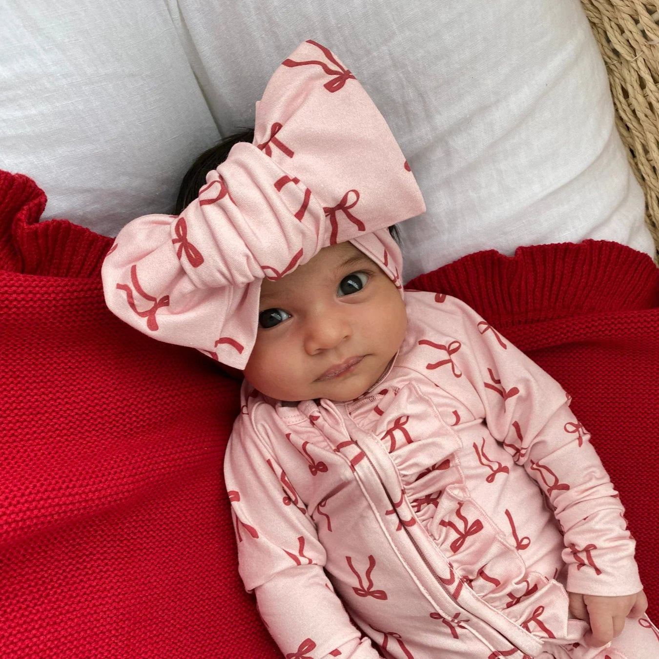 Baby wearing a pink outfit with red patterns on a red blanket