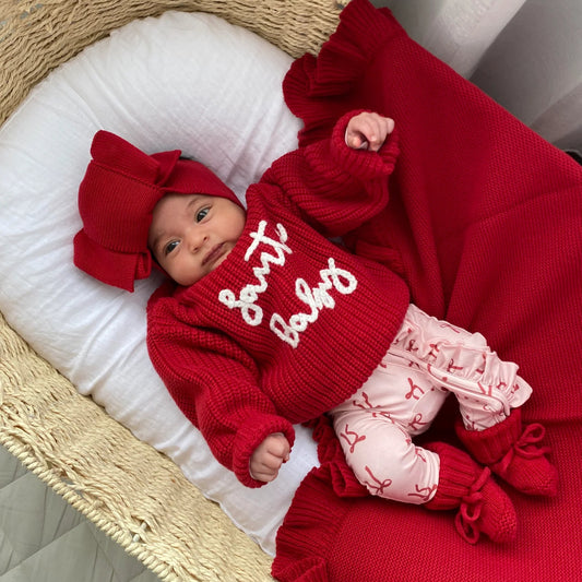Baby in red outfit with 'butter baby' text, lying on a white cushion in a wicker basket.