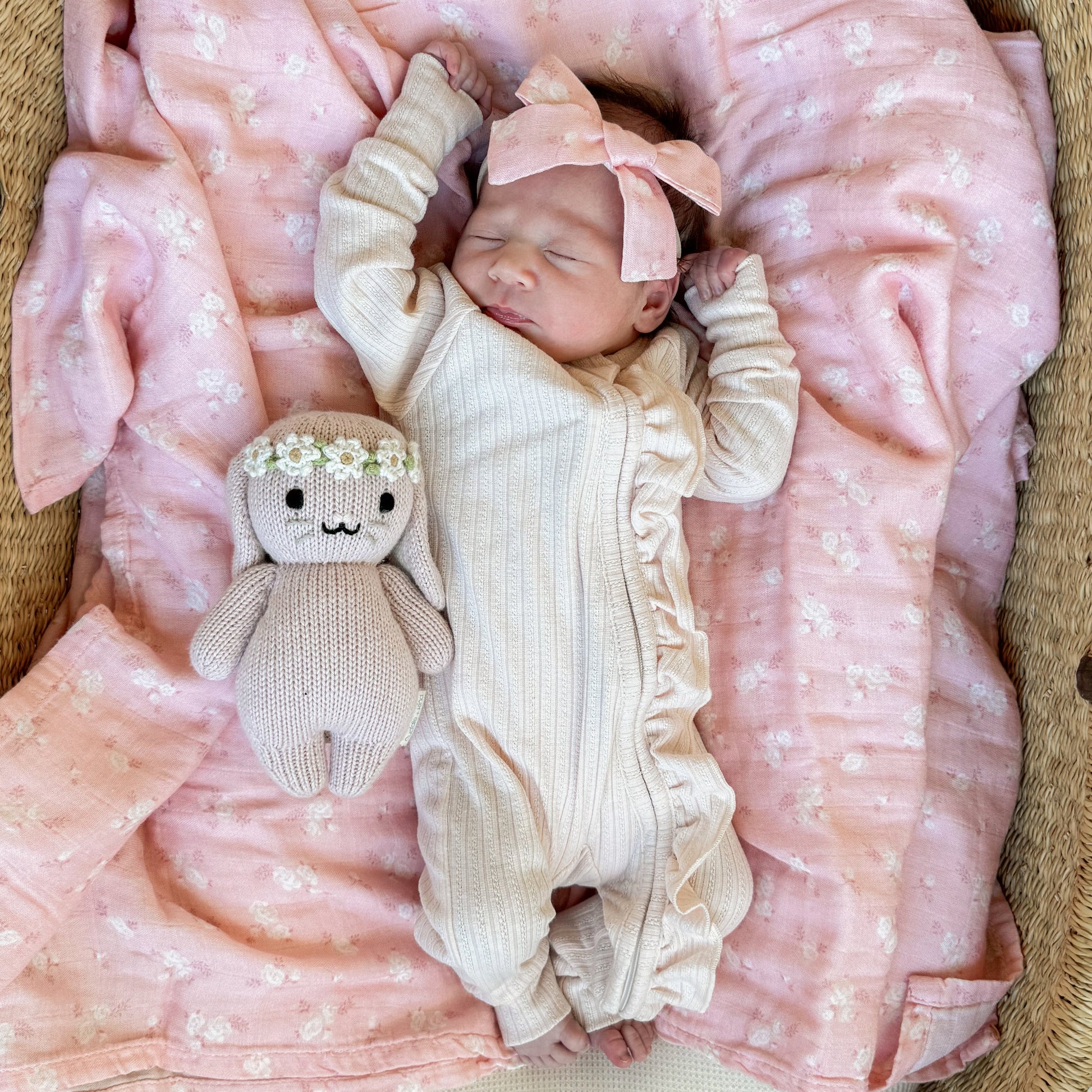 Newborn baby in a crib with pink blankets and a toy, cream frill zip romper