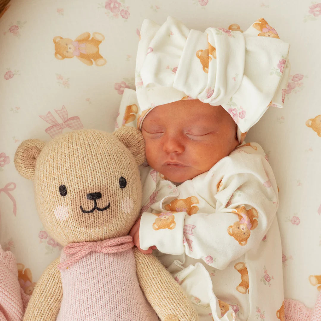 Newborn baby sleeping with a teddy bear on a soft surface with teddy bear pattern