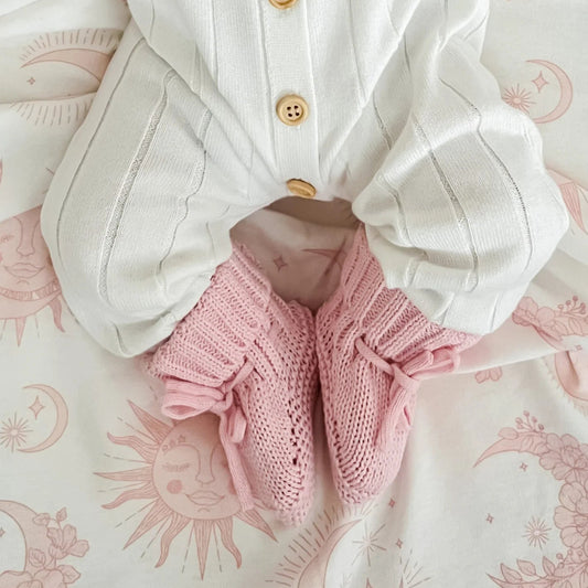White baby outfit with pink knitted booties on a patterned surface